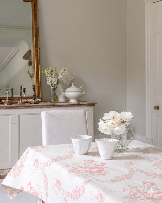 Dining room with a floral tablecloth, white chairs, and decorative items.