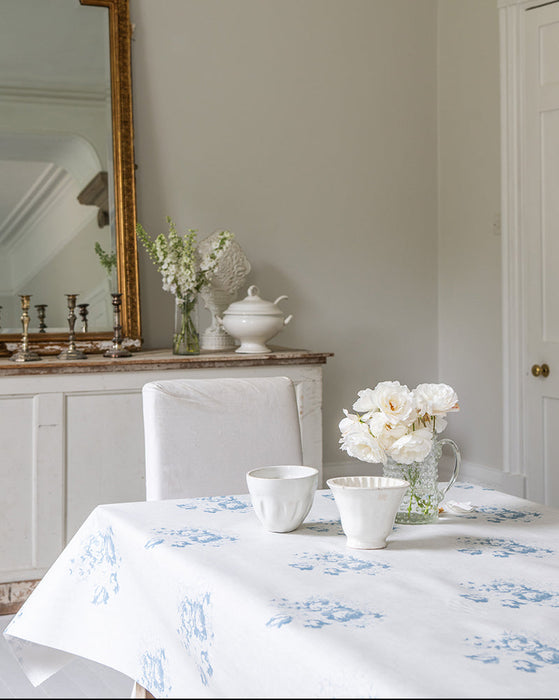 Dining room with a table set for a meal, featuring a floral tablecloth and white tableware.