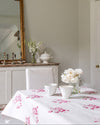 Dining room with a table set with white dishes and flowers, a mirror on the wall, and a vase.
