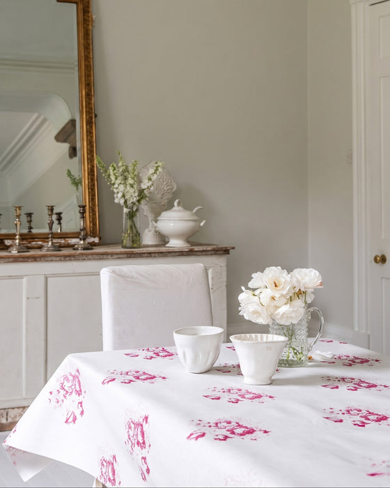 Dining room with a table set with white dishes and flowers, a mirror on the wall, and a vase.