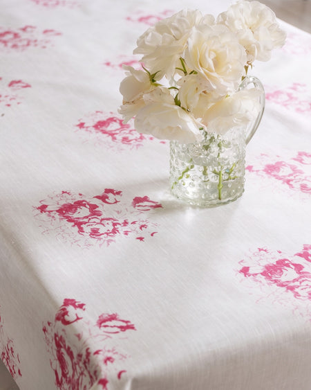 Clear glass vase with white flowers on a tablecloth with pink floral patterns
