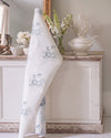 White fabric with blue floral pattern in a room with decorative items on a wooden cabinet.